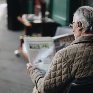 Elderly man reading a newspaper in an outdoor cafe setting, enjoying a peaceful moment.