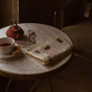 From above of round marble textured table with tea set placed near newspaper and eyeglasses in retro style cafe