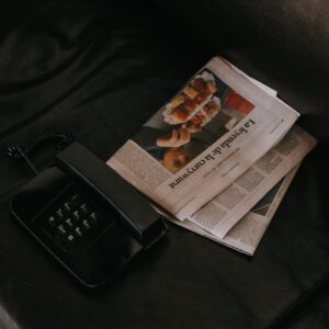 A vintage black telephone and newspaper on a dark leather sofa, conveying a sense of nostalgia.